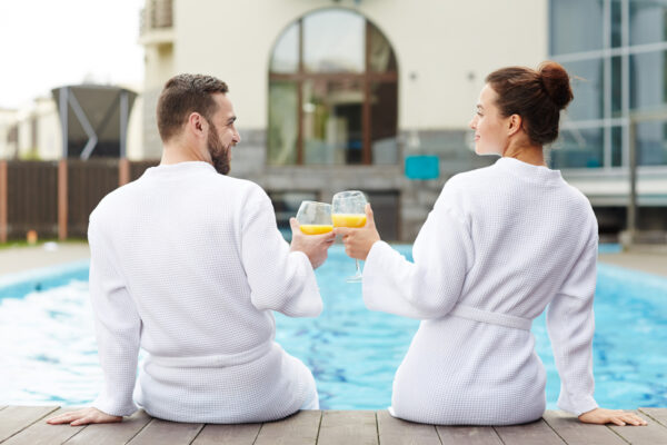 Cuplu în halate albe brindând lângă piscină