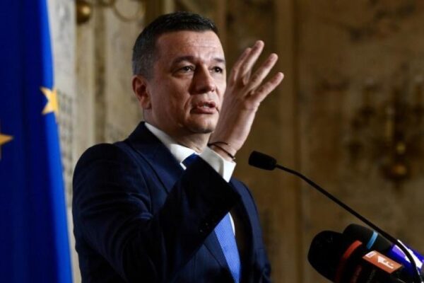 Bărbat în costum vorbind la pupitru, steag UE